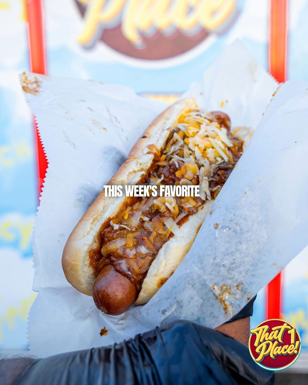 A chili cheese hot dog held in front of the That 1 Place truck